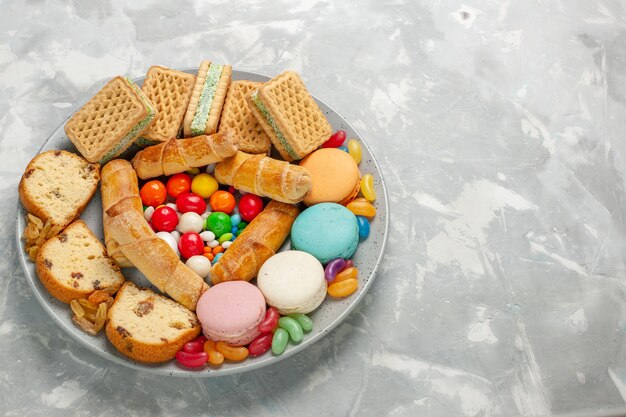 Deliciosos pasteles con macarons y caramelos en mesa blanca