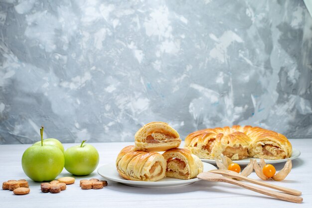 Deliciosos pasteles en rodajas dentro de la placa con relleno junto con manzanas y galletas en el piso blanco galleta pastelería galleta azúcar dulce