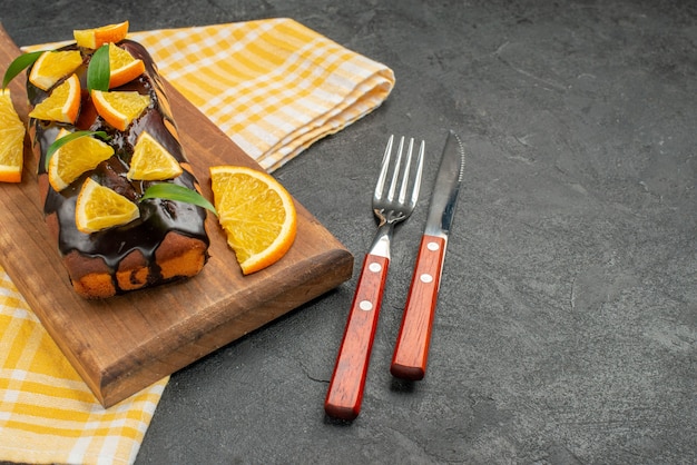 Deliciosos pasteles suaves a bordo y naranjas cortadas con hojas sobre una toalla de rayas verdes de la mesa oscura