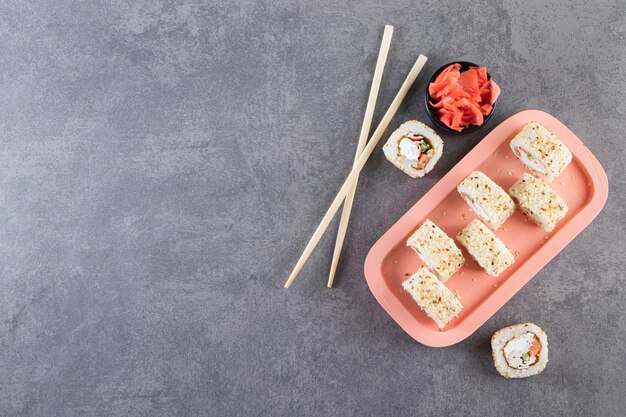 Deliciosos rollos de sushi fresco con salsa de soja y palillos de madera colocados sobre una tabla de madera.