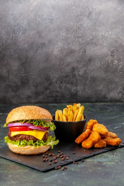 Deliciosos sándwiches caseros papas fritas nuggets de pollo en tablero negro papas fritas pimienta sobre superficie borrosa gris oscuro