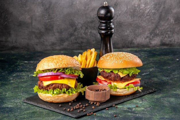 Deliciosos sándwiches caseros en la tabla de cortar negra papas fritas ketchup en la superficie borrosa gris oscuro