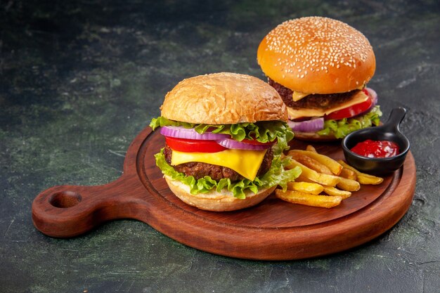 Deliciosos sándwiches papas fritas salsa de tomate en la tabla de cortar de madera sobre la superficie de color mezcla oscura