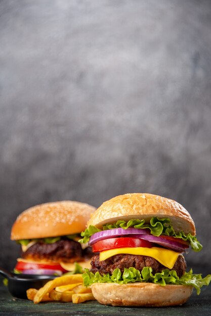 Deliciosos sándwiches papas fritas en la tabla de cortar de madera sobre la superficie de color de mezcla oscura en vista vertical