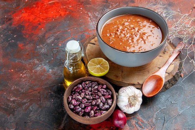 Delicioussoup para cenar con una cuchara y limón en una bandeja de madera, frijoles, ajo, cebolla y botella de aceite en la tabla de colores mezclados