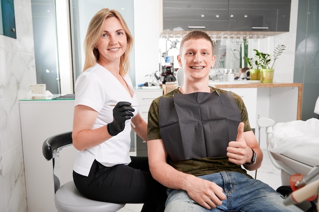 Una dentista alegre y un paciente masculino sentados en el consultorio dental