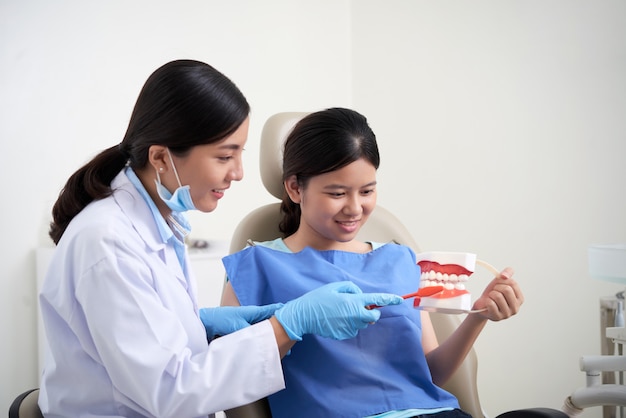 Dentista asiática que demuestra técnica de cepillado de dientes para paciente