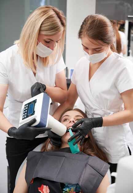 Dentista y asistente examinando dientes de pacientes con máquina de rayos x dental