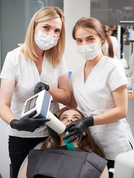 Dentista y asistente examinando dientes de pacientes con máquina de rayos x dental