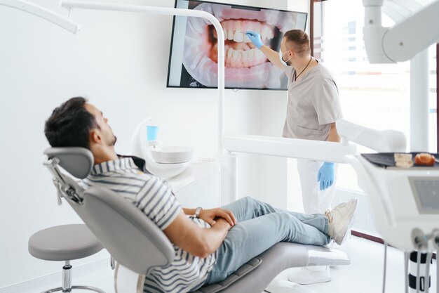 Dentista discutiendo con paciente tendido mostrando la imagen de sus dientes en la pantalla