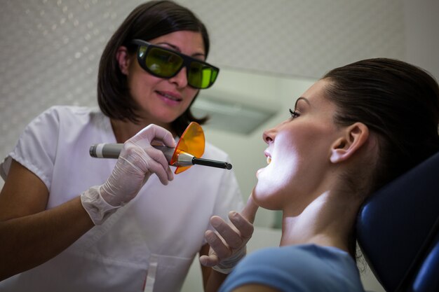 Dentista examina los dientes de los pacientes con luz de curado dental