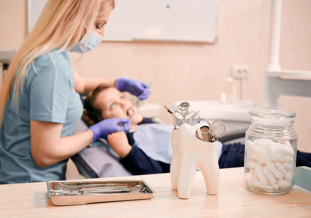 Dentista examinando dientes de niños en gabinete con instrumentos dentales