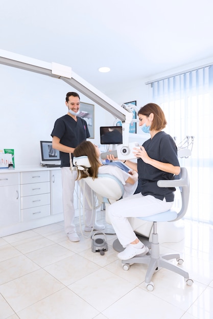 Dentista femenino que explora los dientes del paciente con la máquina de radiografía en la clínica dental moderna
