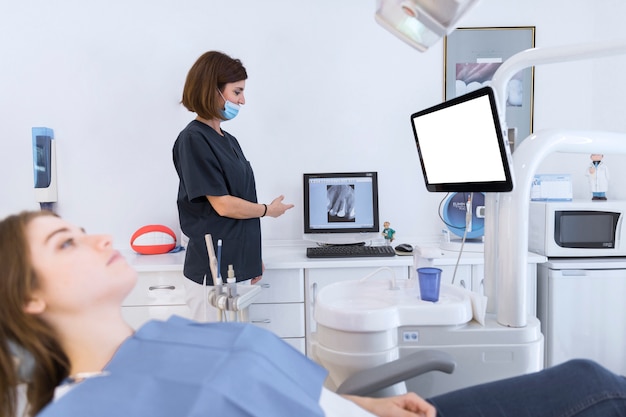 Dentista femenino que muestra la radiografía de los dientes en la computadora en la clínica