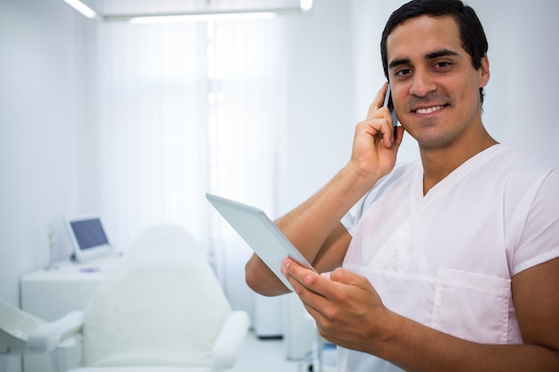 Dentista hablando por teléfono móvil y sosteniendo tableta digital