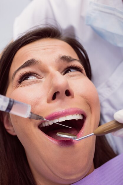 Dentista inyectando anestésicos en la boca del paciente femenino asustado