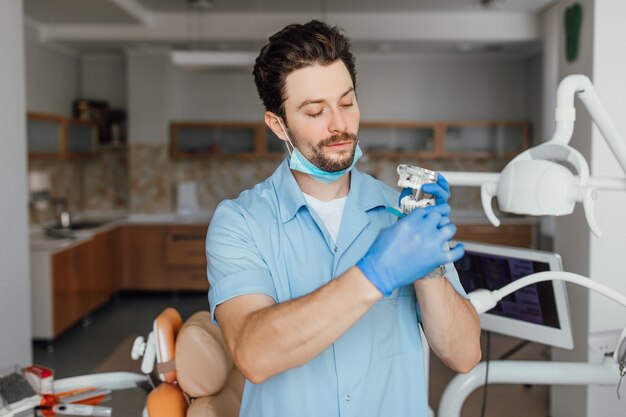 Dentista joven guapo en bata blanca está sosteniendo layot plástico, mientras está de pie en su oficina.