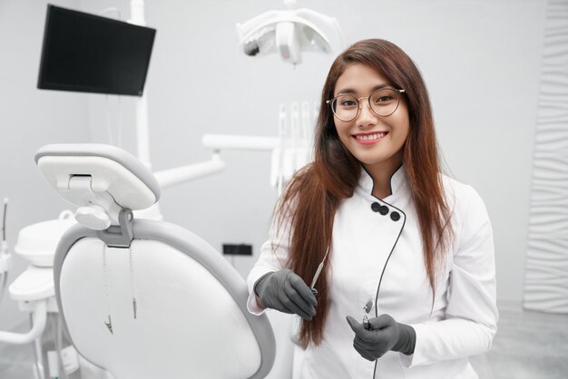 Dentista manteniendo herramientas dentales y sonriendo en la clínica