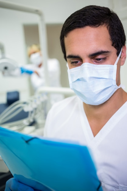 Foto gratuita dentista en mascarilla quirúrgica mirando un expediente médico