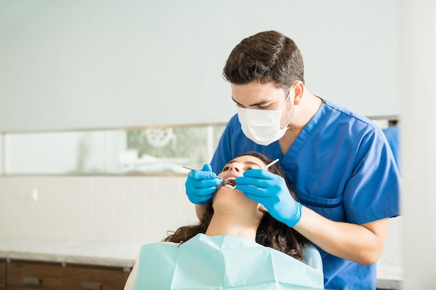 Foto gratuita dentista masculino examinando a una mujer joven con tallador dental en la clínica médica