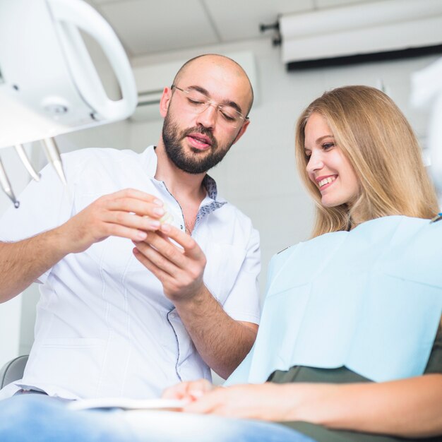 Dentista masculino que muestra la mandíbula dental al paciente femenino feliz