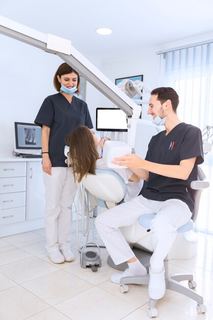 Dentista masculino que se sienta en la silla que explora los dientes del paciente femenino con la máquina de radiografía