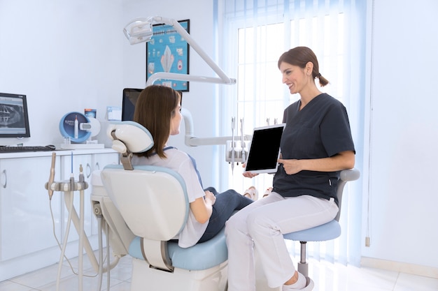 Dentista mostrando tableta digital a paciente femenino en clínica