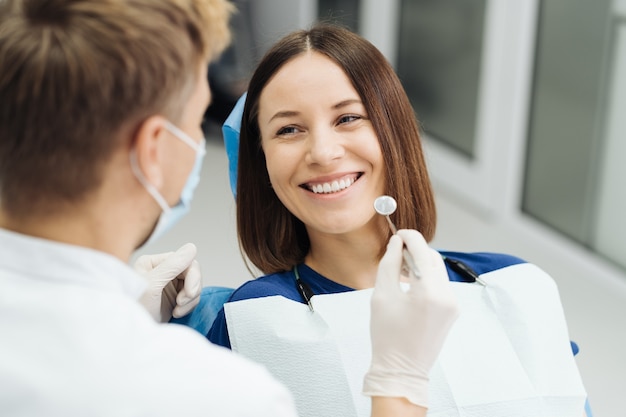 Dentista profesional masculino con guantes y máscara y discutir cómo se verá el tratamiento de los dientes del paciente