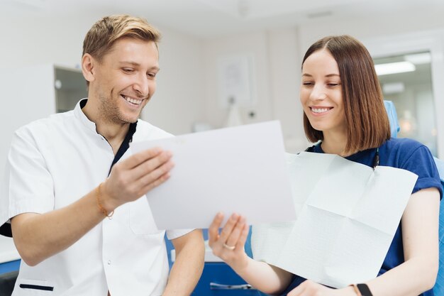 Dentista profesional masculino con guantes y máscara con foto de papeles y mostrar cómo se verá el tratamiento de los dientes del paciente