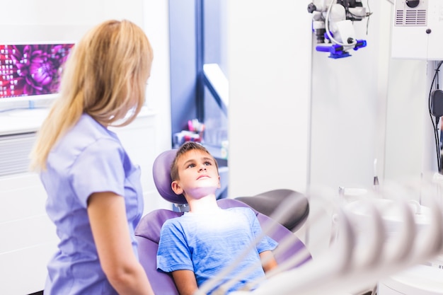 Foto gratuita dentista que se coloca cerca del muchacho que se sienta en silla dental