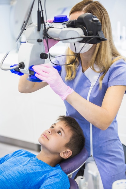 Dentista que comprueba dientes de un muchacho a través del microscopio en clínica