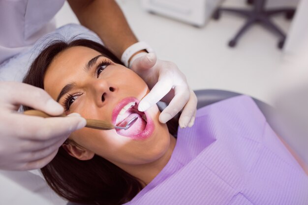 Dentista que examina los dientes del paciente femenino con un espejo de boca