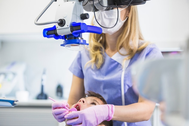 Dentista que examina los dientes del paciente a través del microscopio en la clínica