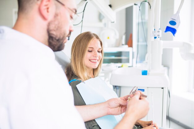 Dentista que mide el modelo plástico de los dientes con el calibrador a vernier cerca del paciente femenino