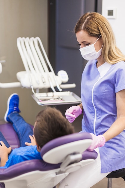 Dentista que mira al paciente del niño que se inclina en silla dental