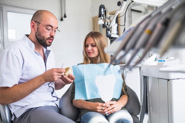 Dentista que trabaja en la mandíbula dental cerca de paciente femenino que se sienta en la silla dental