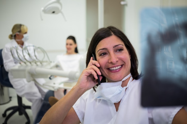 Dentista revisando un informe de rayos X mientras habla por teléfono móvil