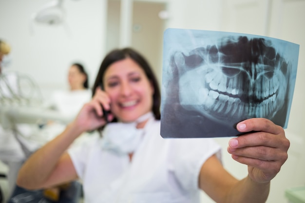 Dentista revisando un informe de rayos X mientras habla por teléfono móvil