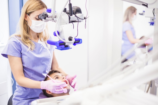 Dentista de sexo femenino joven que examina los dientes del muchacho a través del microscopio