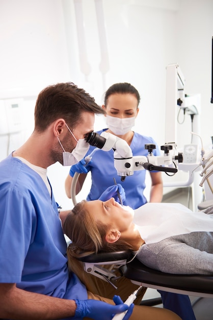 Dentista y su asistente trabajando con microscopio dental