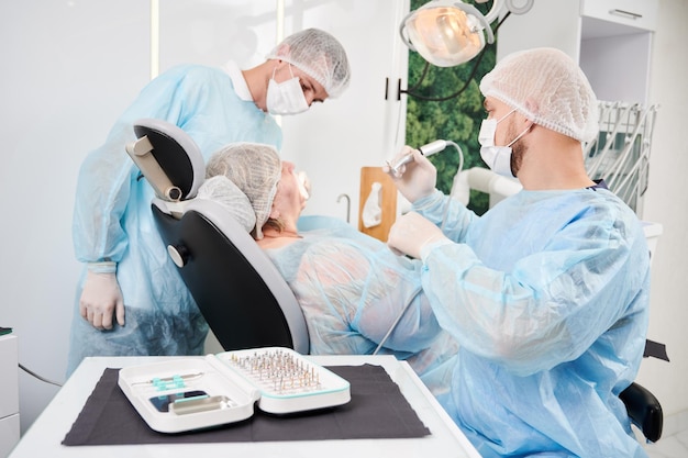 Dentista y su asistente trabajando con un paciente en una silla de dentista en la oficina del dentista