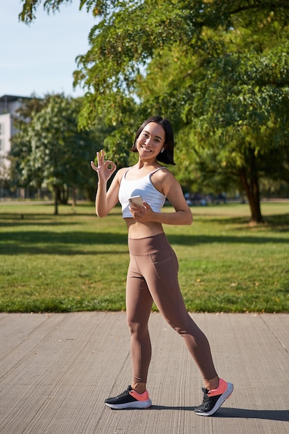 Foto gratuita deporte y bienestar joven deportista en el parque escuchar música y hacer ejercicio sonriente al aire libre trotando