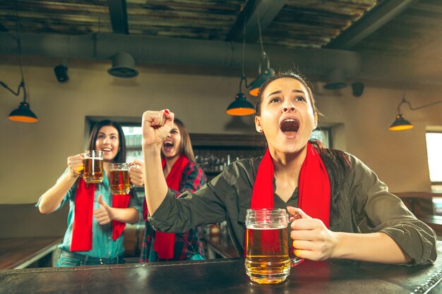 Deporte, gente, ocio, amistad, concepto de entretenimiento: felices fanáticas del fútbol femenino o buenos amigos jóvenes bebiendo cerveza, celebrando la victoria en el bar o pub. Concepto de emociones positivas humanas