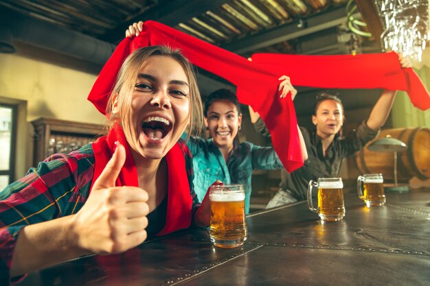 Deporte, gente, ocio, amistad, concepto de entretenimiento: felices fanáticas del fútbol femenino o buenos amigos jóvenes bebiendo cerveza, celebrando la victoria en el bar o pub. Concepto de emociones positivas humanas