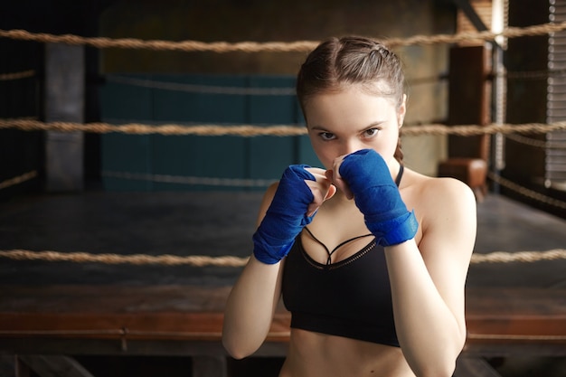 Deportes, determinación, fitness y artes marciales. Deportiva chica vestida de negro dry fit top y vendas de boxeo de pie en postura defensiva,