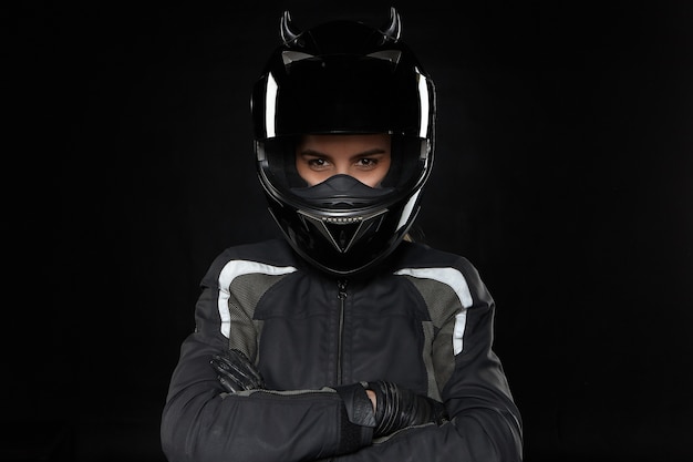 Deportes de motos, extremos, competición y adrenalina. Corredor femenino joven activo con casco protector y uniforme que va a participar en carreras de carretera o motocross, cruzando los brazos sobre el pecho