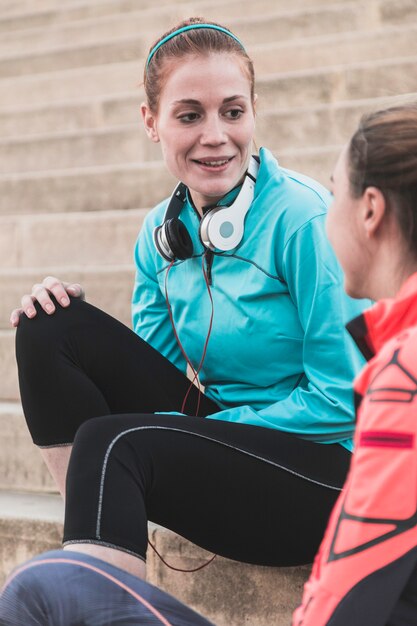 Deportista con auriculares alrededor de su cuello sentada en las escaleras