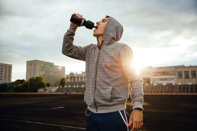 deportista bebiendo agua después de correr, hacer ejercicio, con auriculares