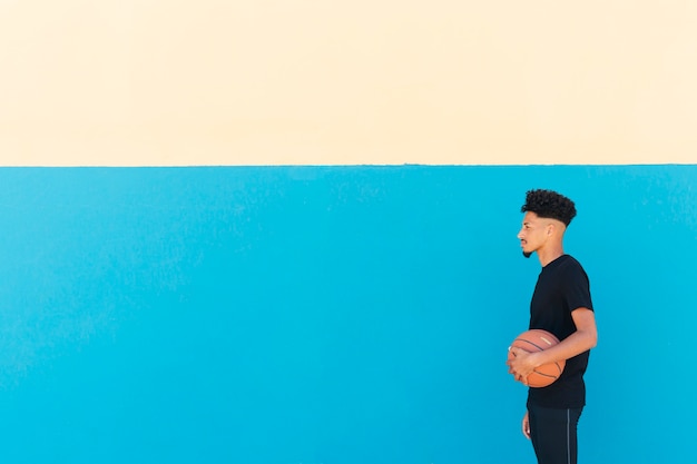 Deportista étnico con el pelo rizado de pie con el baloncesto.