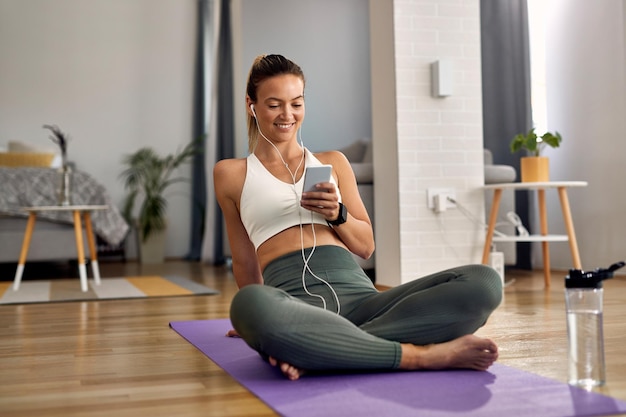 Deportista feliz usando un teléfono inteligente mientras se relaja después de hacer ejercicio en casa